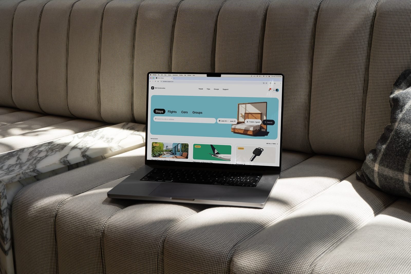 MacBook on a sofa open to Engine, with Stays, Flights, Cars, and Groups search